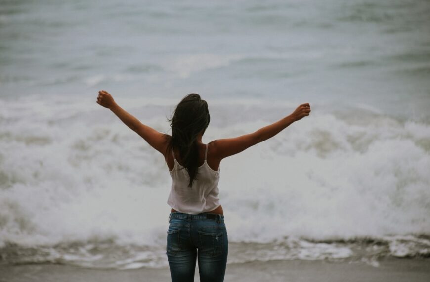 A person standing with their arms in the air in front of a wave