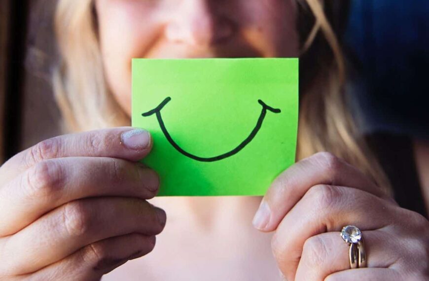 woman holding a sticky note with a smile drawn on it