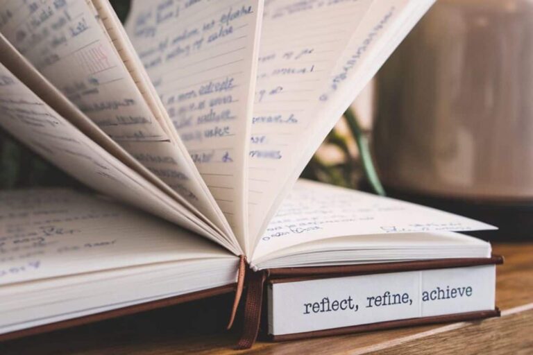 journal open with the words reflect, refine, achieve