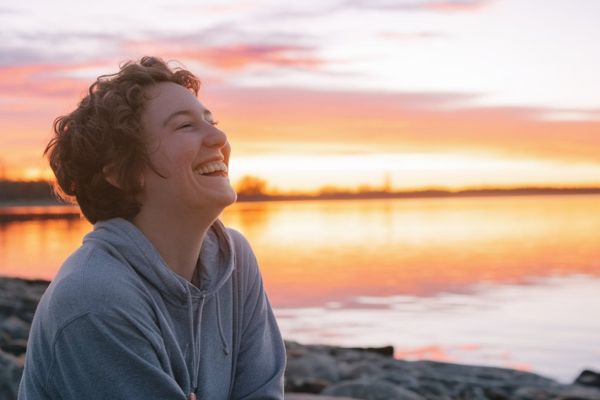 a person smiling and looking up at the sunrise on a beach